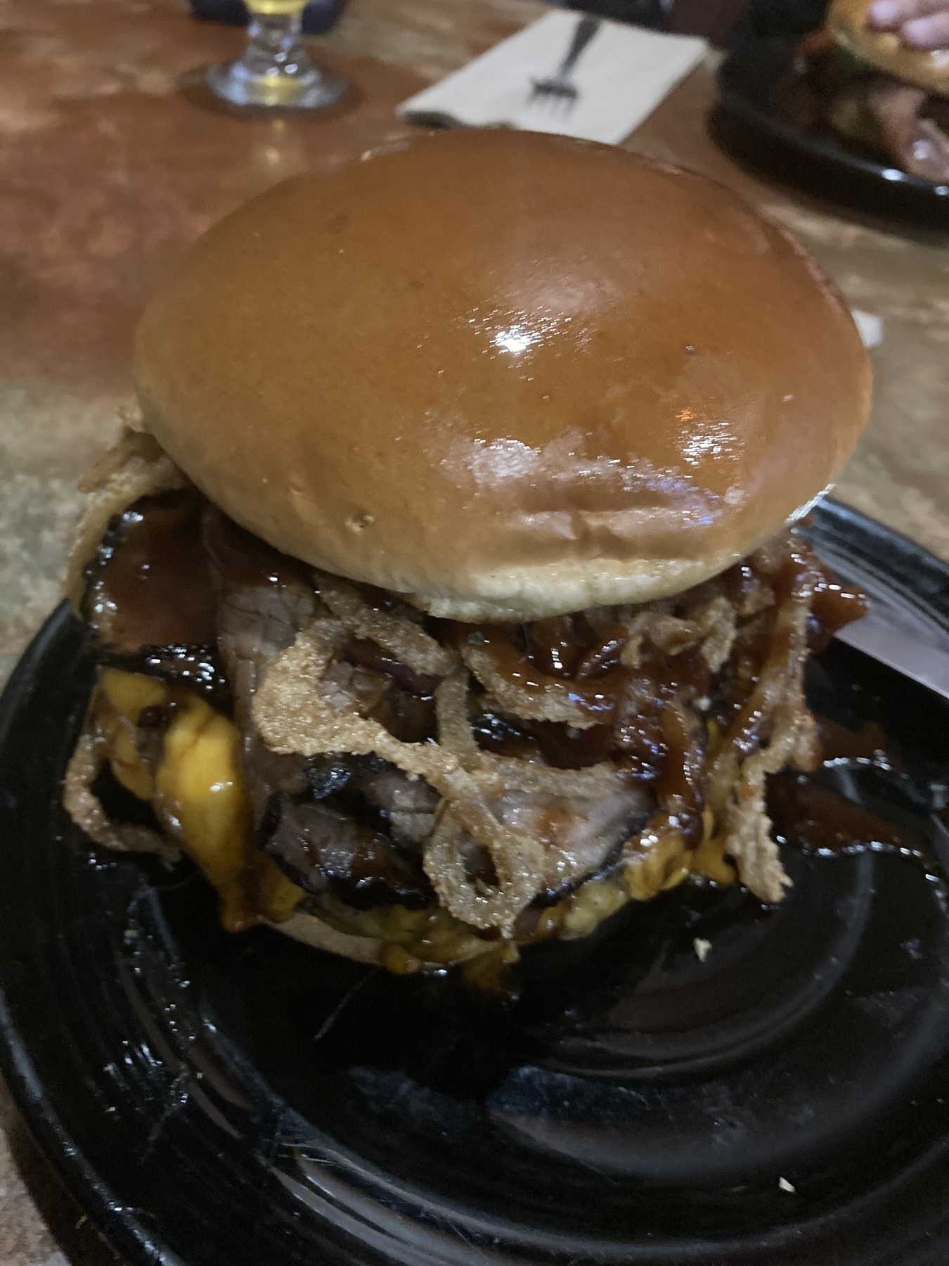 A huge burger with bbq sauce, roast beef, cheddar cheese, and onion rings. 